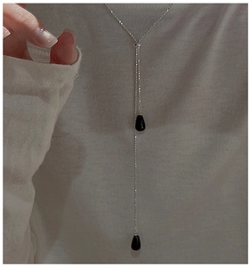 Détail d'un collier long en Y argenté avec deux pendentifs gouttes noirs portés par un mannequin