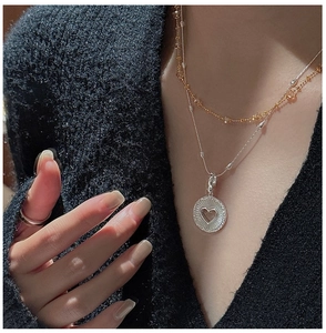 Détail de chaînes superposées en or et argent avec pendentif pièce en forme de coeur