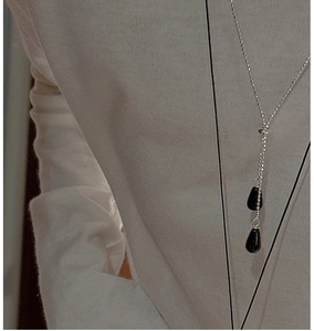 Détail du collier à billes argenté avec double pendentif goutte noire sur un mannequin