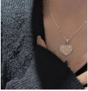 Close-up of pink heart pendant with star details worn on a black sweater neck