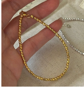 Macro detail of faceted S925 sterling silver beads with lobster clasp on a gold bracelet
