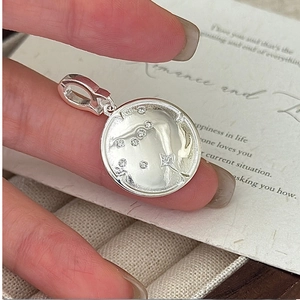 Vue macro d'un pendentif disque constellation en argent S925 tenu dans la main