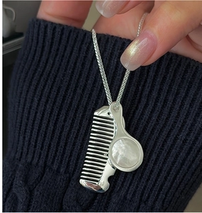 Detail of silver mirror and comb pendant necklace on a black knit sweater background
