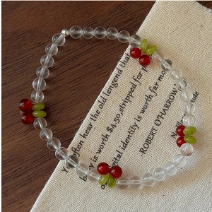 Detail shot of cherry beaded bracelet with red fruit and green leaves on rustic background