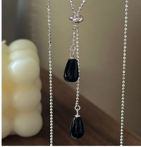 Détail d'une chaîne à billes argentée avec pendentif goutte noir sur fond de bois