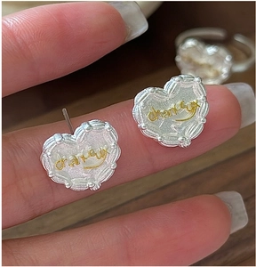 Macro detail of S925 silver heart earring with golden chanceux text and beaded edge