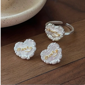 Macro view of heart-shaped silver and gold earrings and ring set with chanceux engraving