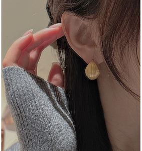 Macro shot of gold shell-shaped earrings with radial textures on a model's ear