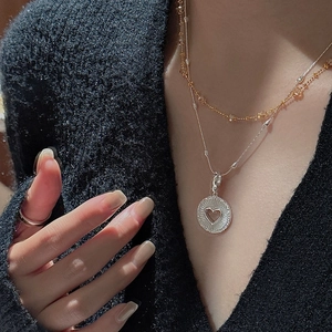 Colliers superposés avec perles dorées et pendentif cœur sur un pull en tricot noir