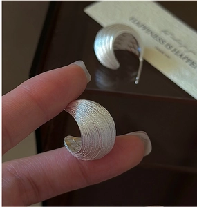 Detailed macro view of silver C-shaped earrings with textured brushed metal finish