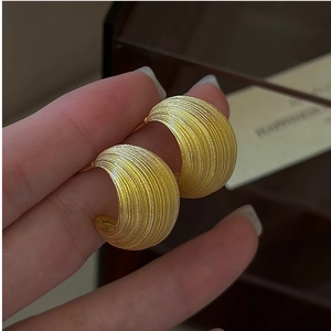 Detail of golden C-shaped earrings with fine texture shown against a gift box