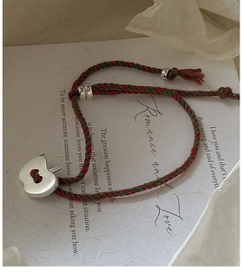 Détail d'un bracelet tissé rouge et vert avec un pendentif pomme argenté sur carte romantique