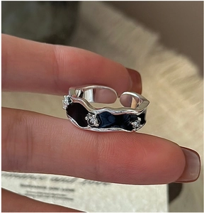 Close-up of irregular wave silver ring with black enamel and three small sparkling zircons