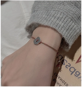 Détail du bracelet tressé rouge et vert avec pendentif pomme en argent sur manche en tricot