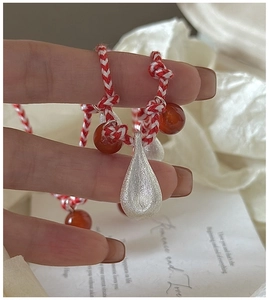 Close-up of S925 silver water drop pendant on a red and white woven cord necklace