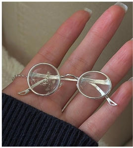 Vue macro d'un mini pendentif lunettes rétro en argent tenu dans la main pour taille