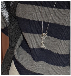 Détail d'un collier pendentif lunettes en argent S925 porté sur un pull à rayures
