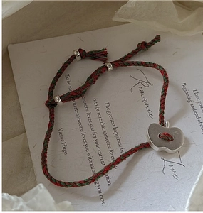Détail d'un bracelet tressé rouge et vert avec un pendentif pomme en argent sur carte poétique