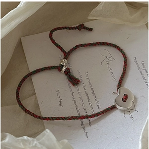 Détail du bracelet tressé rouge et vert avec un pendentif en forme de pomme argentée
