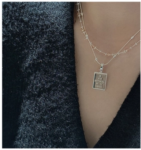 Macro detail of S925 silver necklace with engraved rectangular tag and layered beaded chain