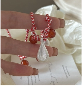 Macro detail of S925 silver matte teardrop pendant on red and white woven cord necklace