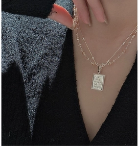 Detail of gold double-layered necklace with engraved rectangular pendant on model