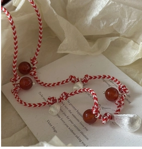 Detail of red and white woven cord necklace with red agate beads and silver pendants