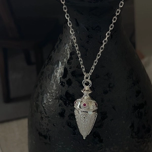 S925 Silber Retro-Halskette mit strukturiertem Anhänger und roten Steinen auf schwarzer Vase