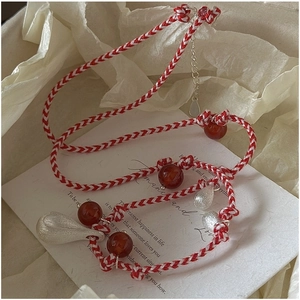 Detail of woven red cord necklace with silver teardrop pendant and garnet beads