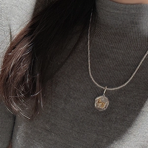 Detailed view of a retro silver and gold horse coin pendant on a grey knit sweater