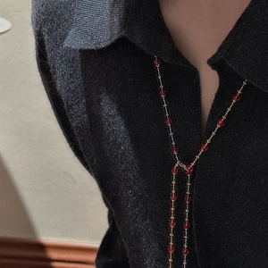 Detail of Y-shaped S925 silver necklace with red beads on a black knit sweater