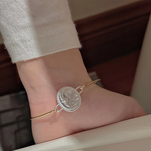 Detail of vintage embossed silver medallion with gold chain worn on female ankle