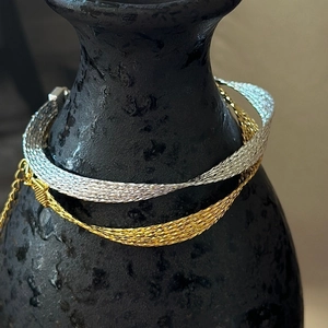 Elegant gold and silver braided snake chain bracelets displayed on a minimalist dark vase
