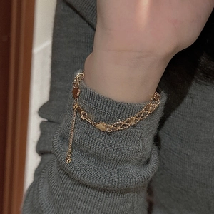 Detail of layered gold lace bracelet with heart charm on a grey sweater sleeve
