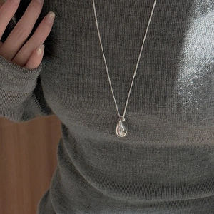 Macro shot of a polished silver teardrop pendant on a fine chain over a knit sweater