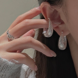 Détail de boucles d'oreilles en maille argentée et bague torsadée portées par mannequin