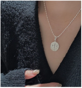 Gros plan d'un pendentif croix rétro en argent porté sur un pull en maille noire au style épuré