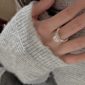 Detailed view of an S925 sterling silver knotted ring on finger with knit sweater background