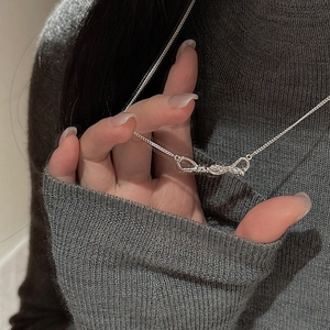 Close-up of a silver-tone knotted bow pendant on a fine metal chain necklace