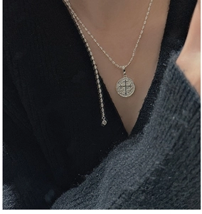 Vue détaillée d'un pendentif pièce en argent S925 vintage avec croix sur un pull noir