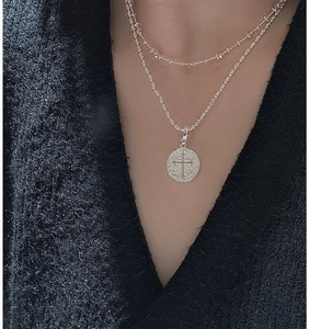 Détail d'un collier S925 en argent à double rang avec pendentif croix sur un pull v