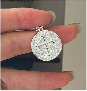 Gros plan d'un pendentif croix rétro en argent avec texture mate tenu à la main