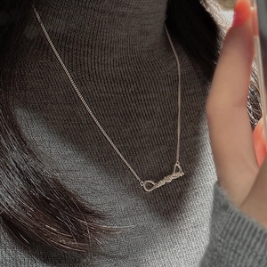 Detail of silver S925 knotted necklace worn on a grey knit turtleneck sweater