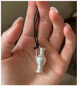 Macro detail of a vintage matte S925 silver vase pendant on a black cord held in hand