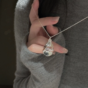 Close-up of a silver teardrop pendant with a mirror finish on a delicate chain necklace
