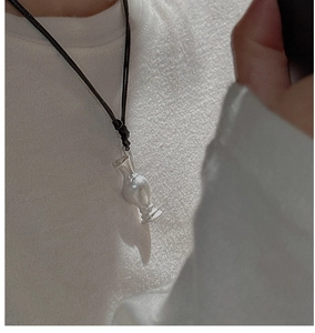 Detailed view of silver vase-shaped pendant on black cord over white t-shirt