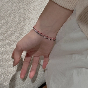 Detailed view of layered red and black woven cord bracelet with silver chain on wrist