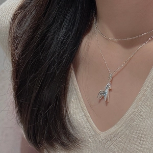 Detail of silver S925 pony pendant necklace worn on a neck with a v-neck sweater