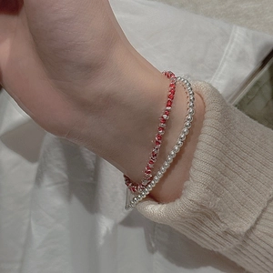 Detail of red braided rope bracelet and silver beads layered on a knit sleeve