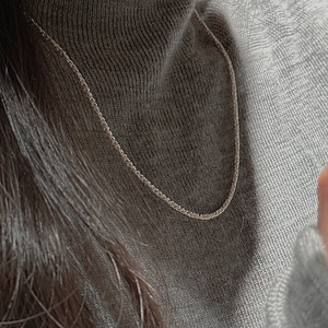 Close-up of minimalist S925 sterling silver twisted rope chain on a grey sweater